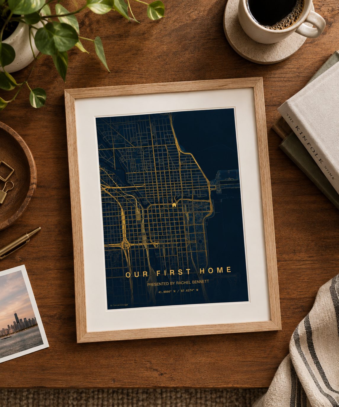 Flat lay of a framed LJ Map Co "Our First Home" map print on a wood table beside a coffee cup and a Chicago skyline photo